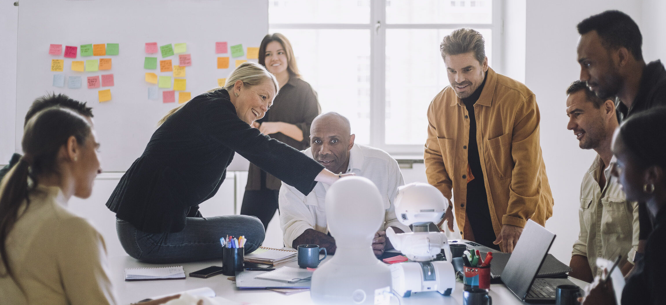 AI i designpraktiken Ett team av personer interagerar nyfiket med en människoliknande robot.